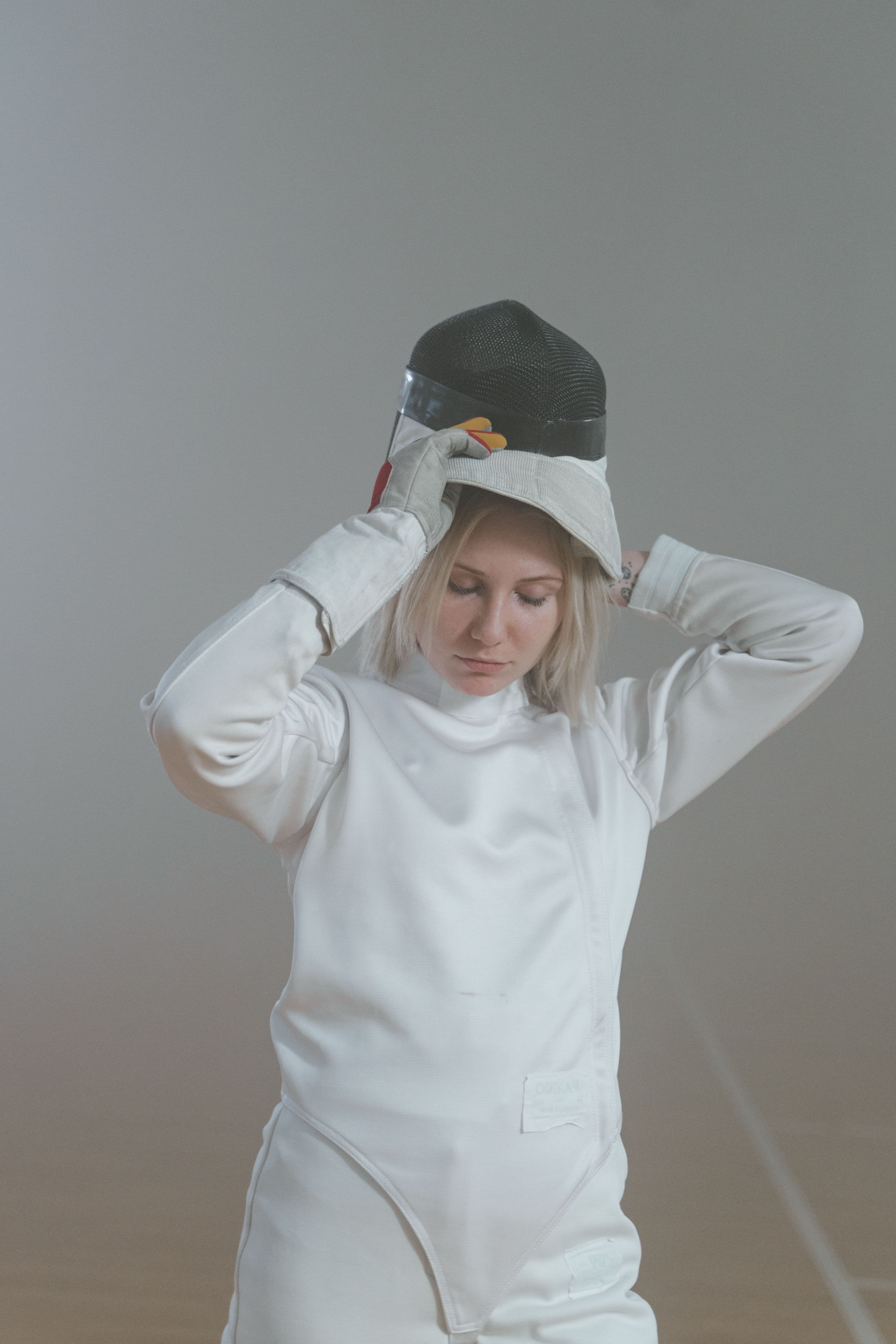 Fechterin in weißer Fechtkleidung mit Jacke, Hose und Handschuh.